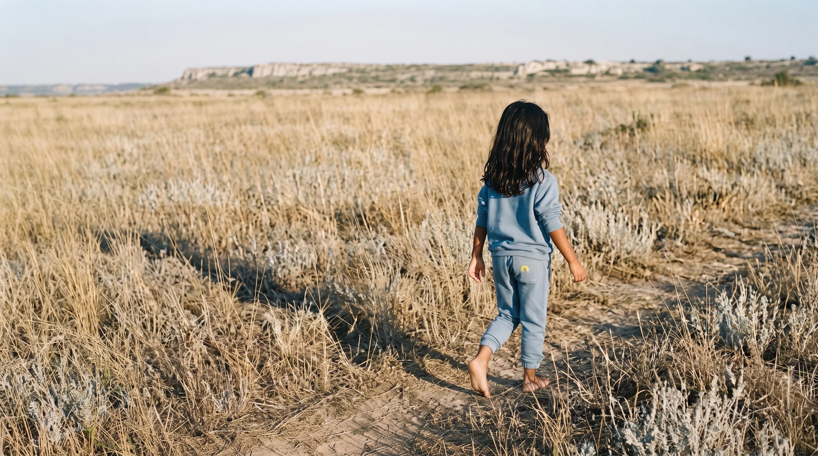 A child walking through a field of tall grass at dawn.