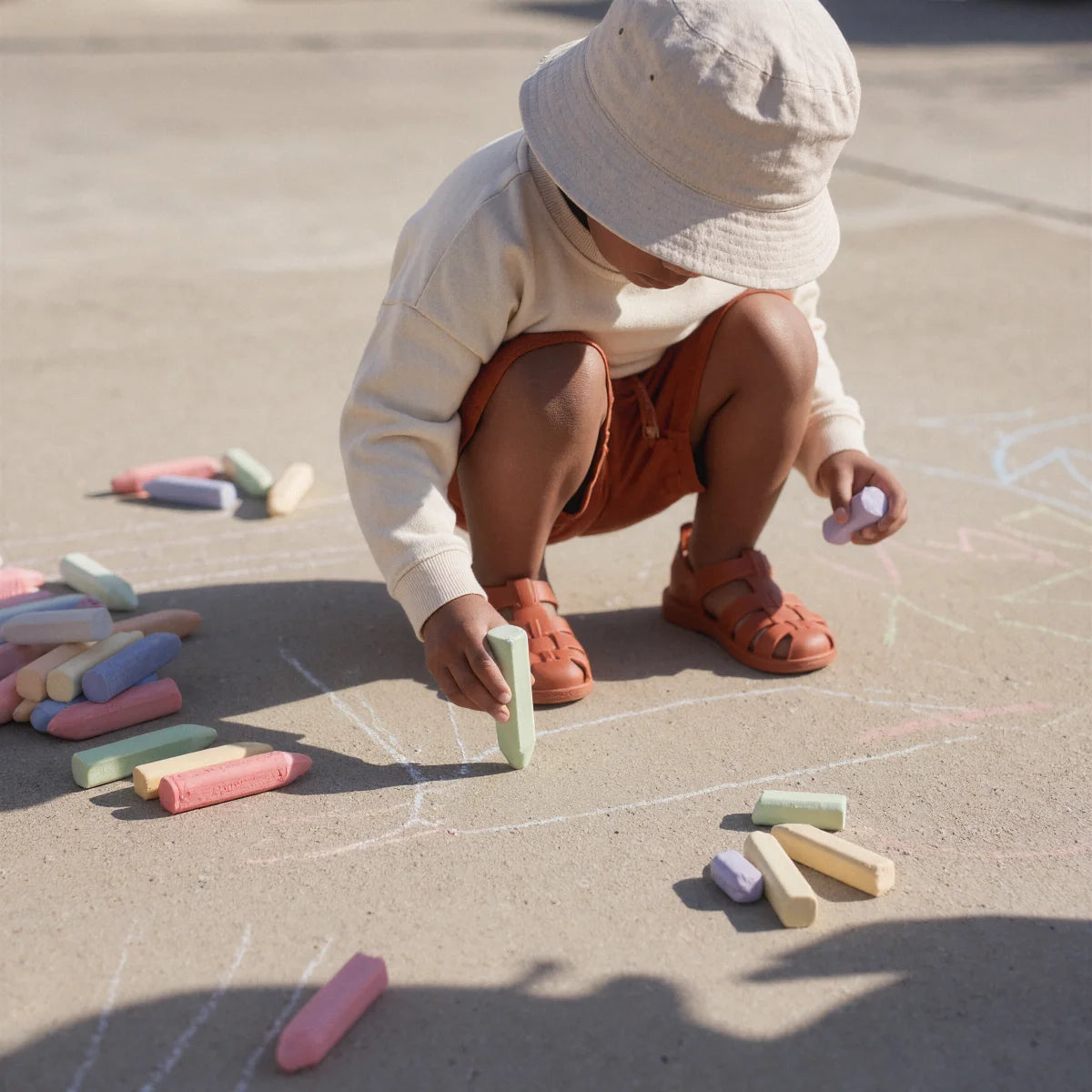 A child crouched down, absorbed in painting on the ground using a chalk
