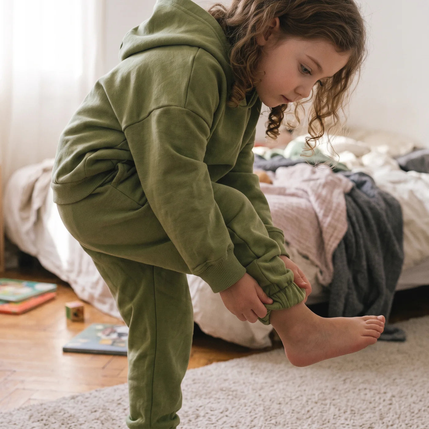 A toddler pulling on their own shorts in soft morning light.