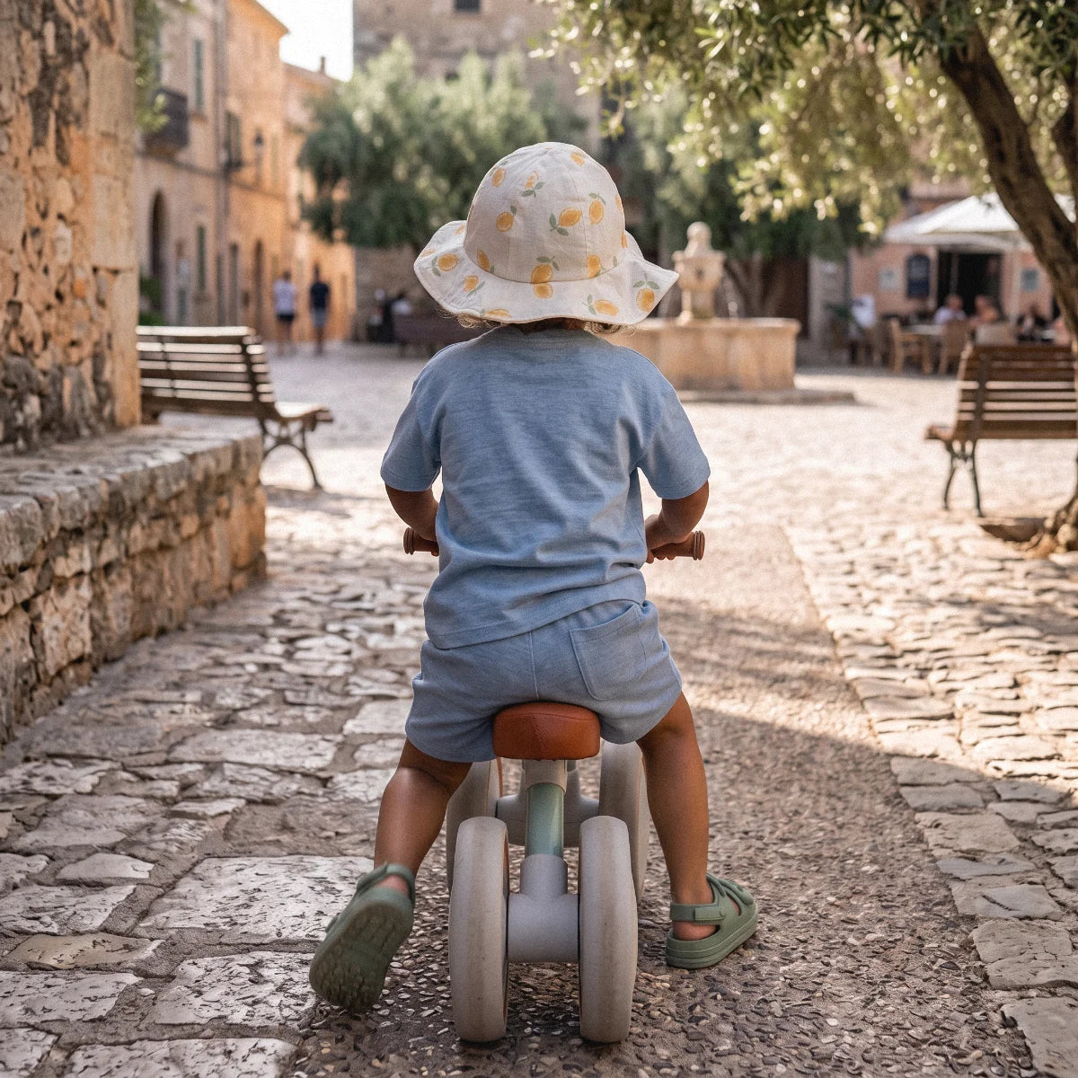 A toddler riding a balance bike during a summer morning stroll.